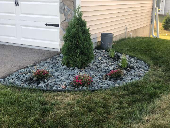 Rock bed with black edging and small plantings at the corner of a garage