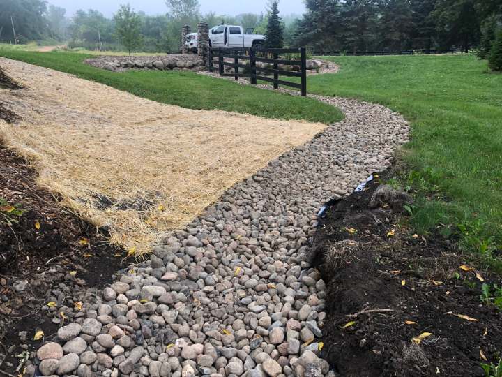 River rock channel curving through a lawn beside a graded slope covered with straw blanket