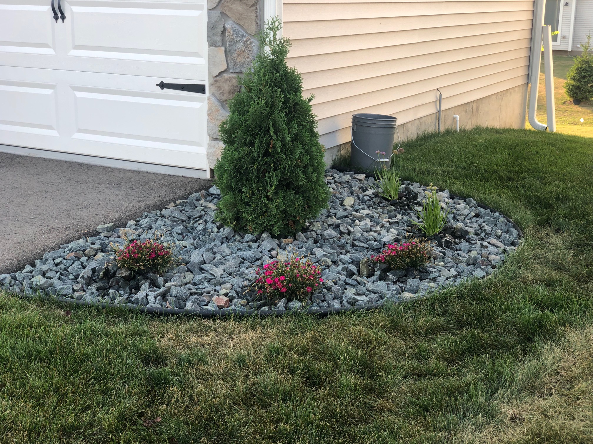 Rock bed with black edging and small plantings at the corner of a garage