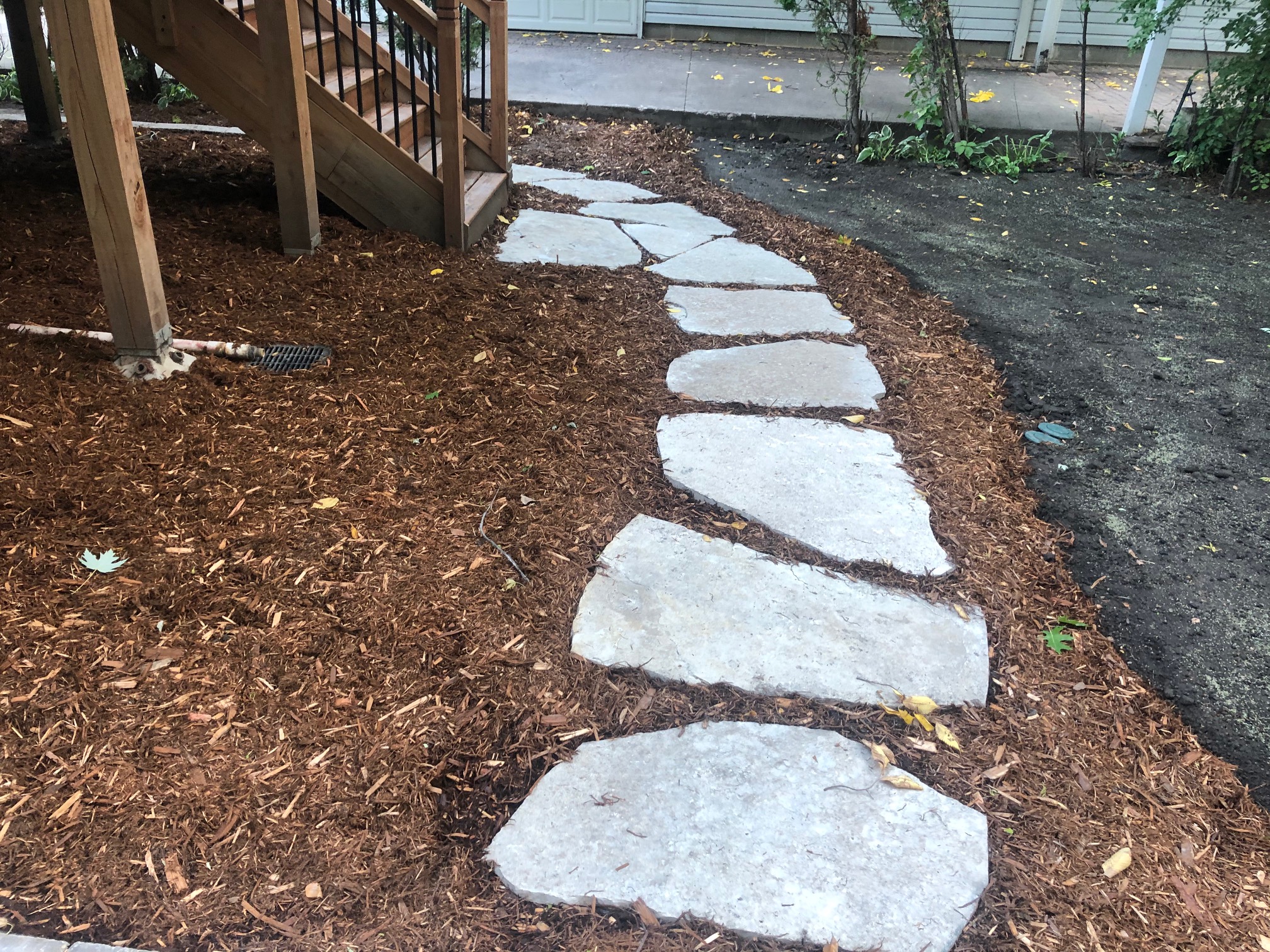 Flagstone stepping stones set into a fresh mulch bed beside deck stairs