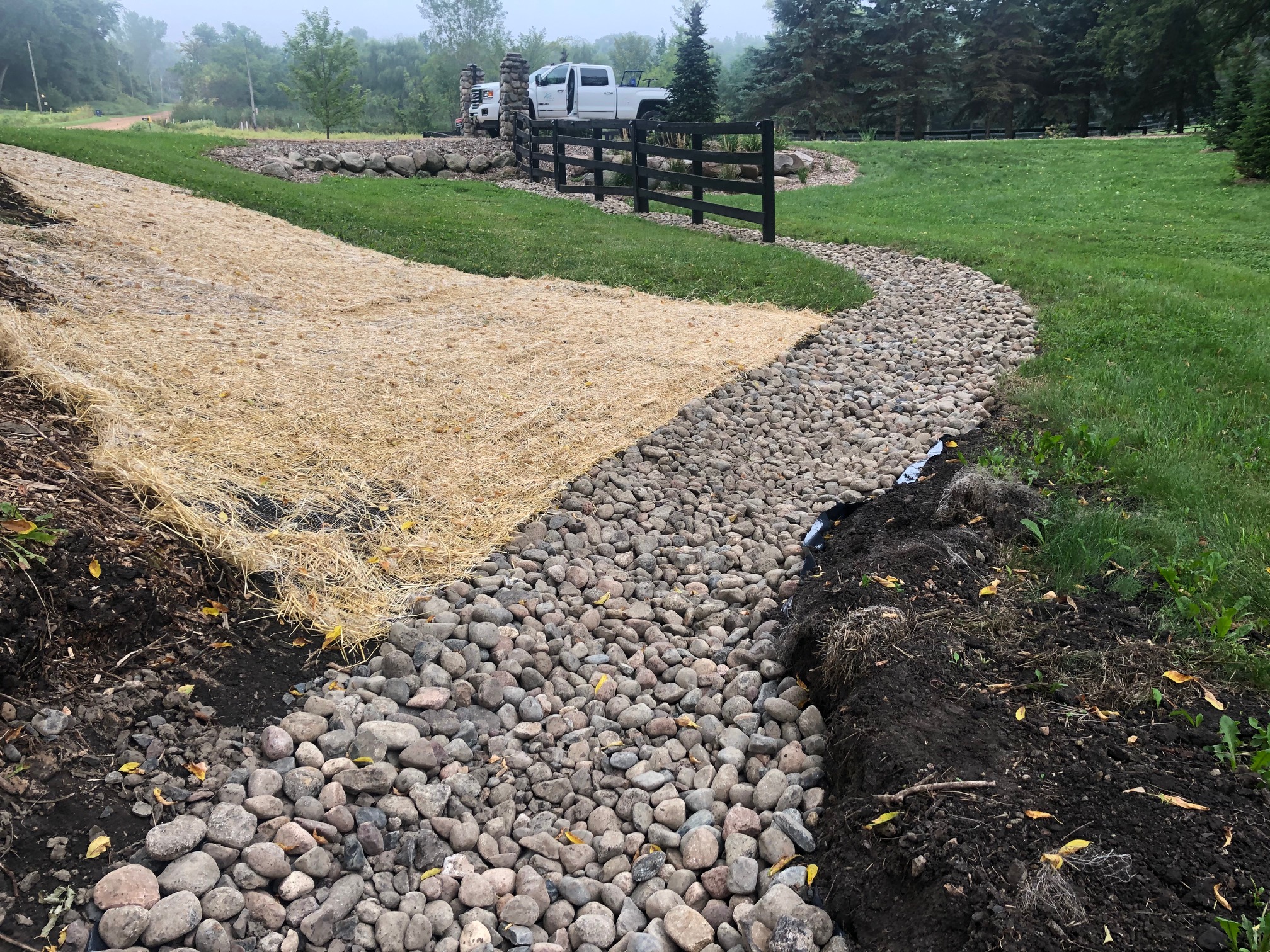 River rock channel curving through a lawn beside a graded slope covered with straw blanket